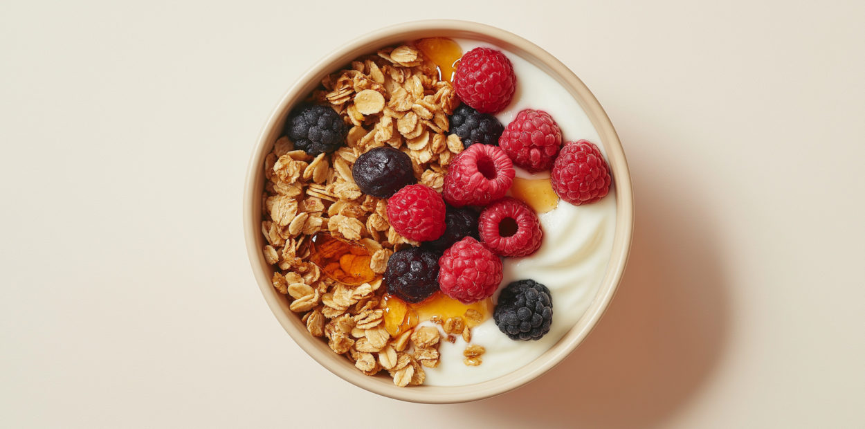 a bowl of fresh granola with greek yogurt topped with honey and fresh berries against an isolated light beige background