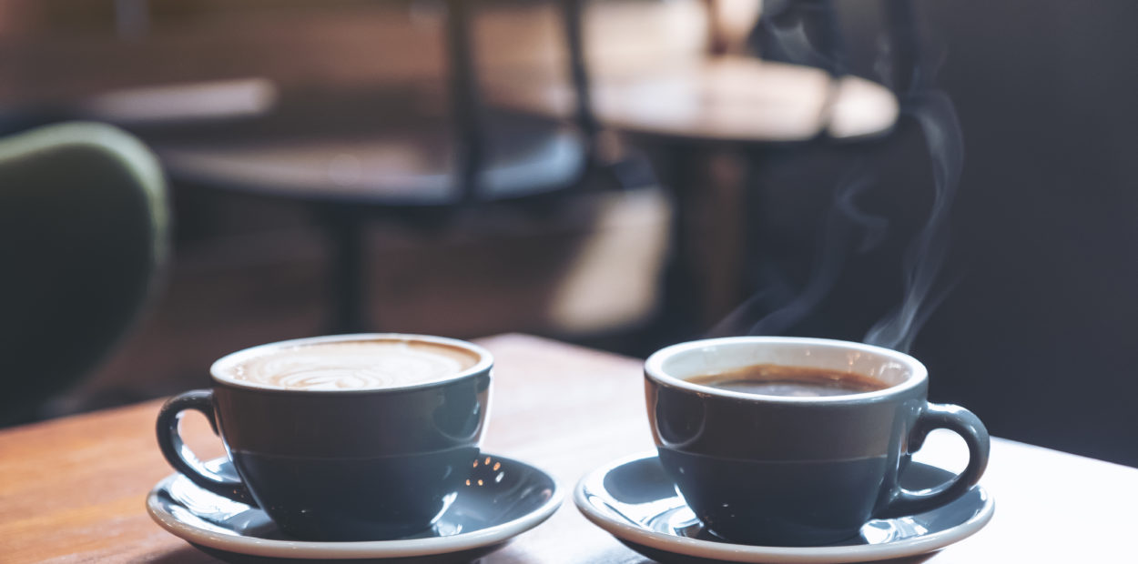 Closeup image of two blue cups of hot latte coffee and Americano coffee on vintage wooden table in cafe